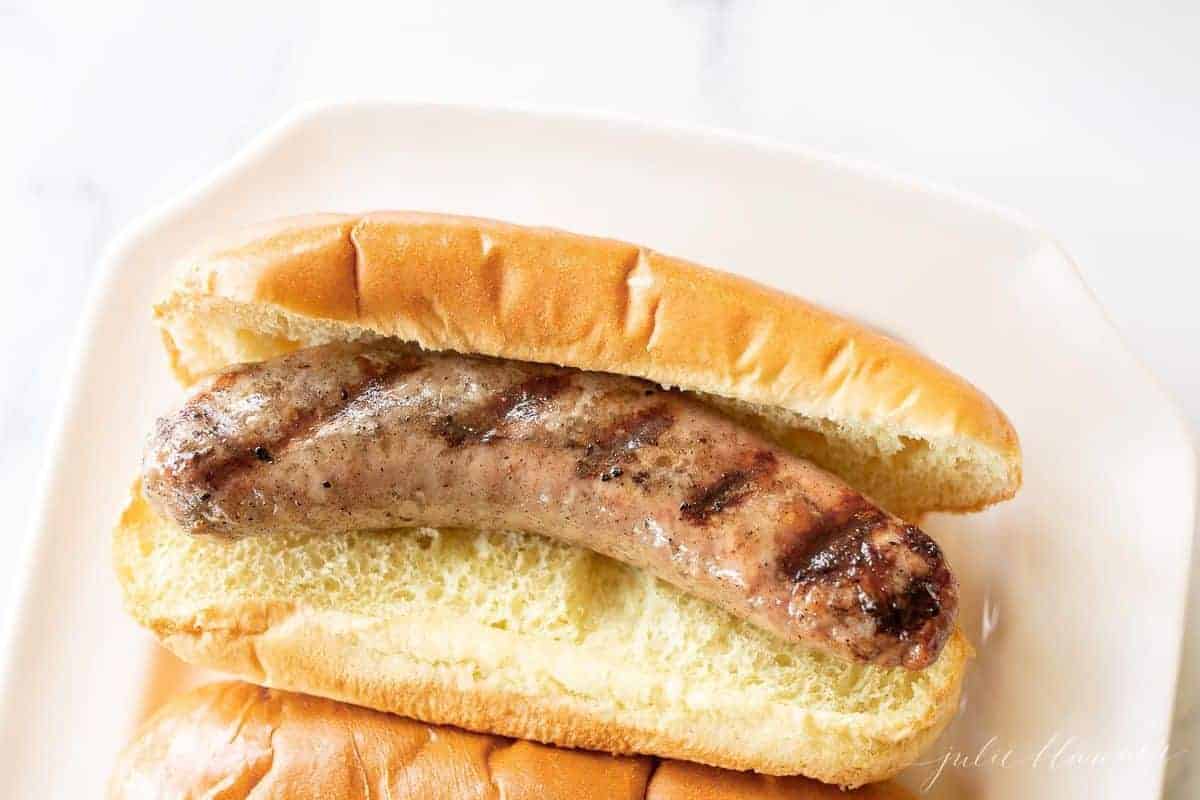 A white tray filled with bratwurst sausages in buns.