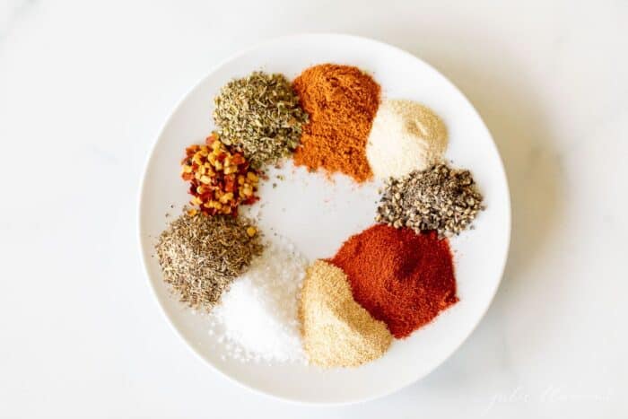 A white plate with piles of spices to make cajun seasoning.