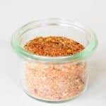 A marble surface with a small glass jar full of cajun seasoning.