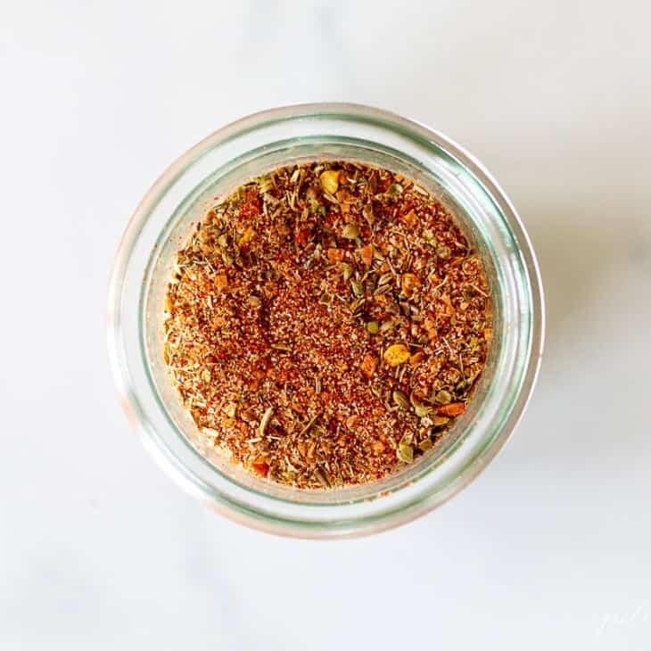A marble surface with a small glass jar full of cajun seasoning.