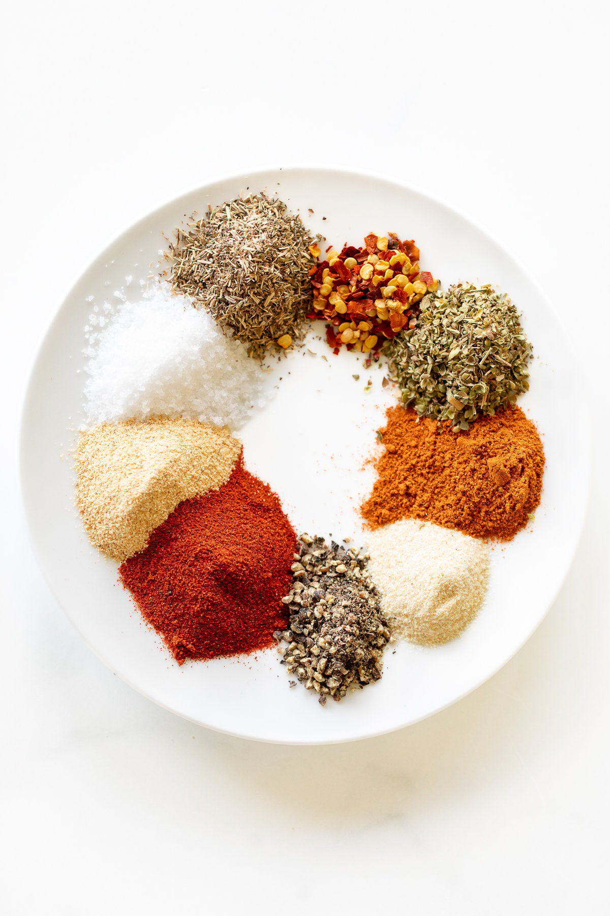 Various spices on a white plate for a homemade cajun seasoning recipe.