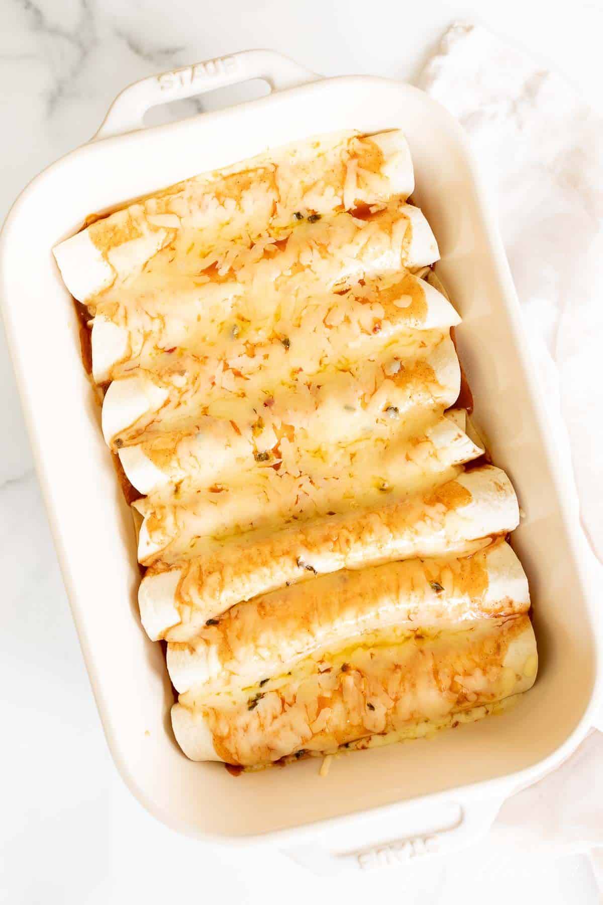 A white casserole dish filled with cheese enchiladas.