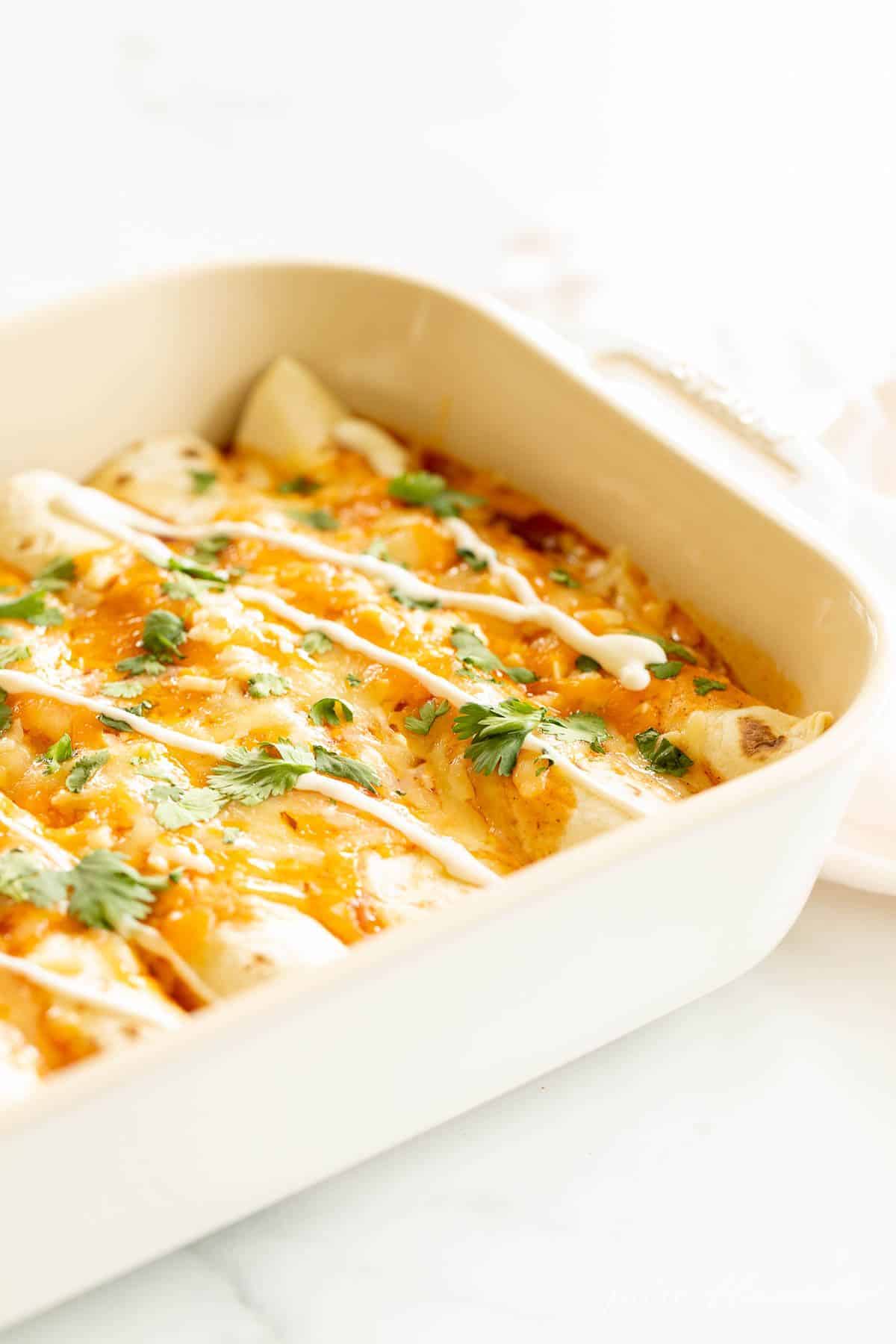 A white casserole dish filled with chicken enchiladas topped in melted cheese.