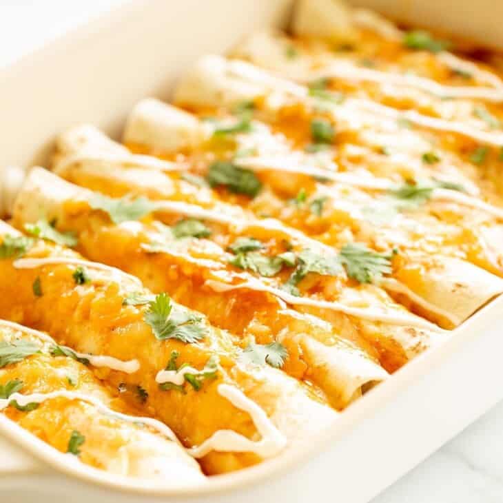 A white casserole dish filled with chicken enchiladas topped in melted cheese.