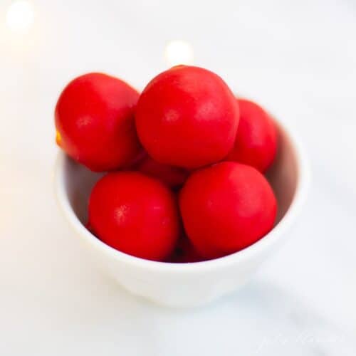 A white bowl full of red coated cookie dough balls for Christmas.