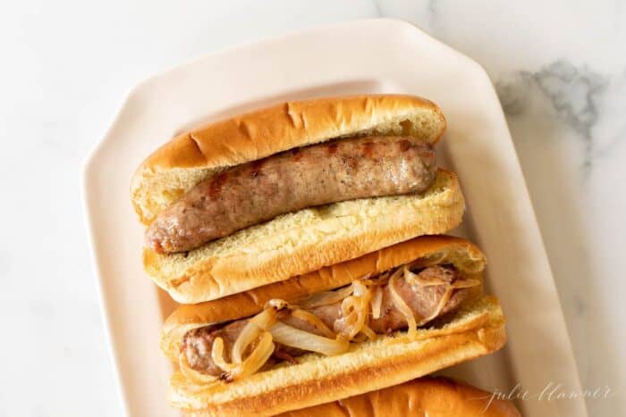 A white tray filled with bratwurst sausages in buns.