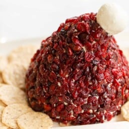 A Cranberry cheeseball in the shape of a Santa hat, surrounded by crackers on a white platter.