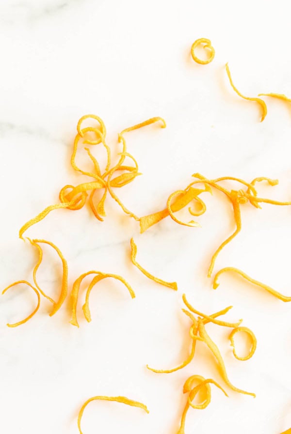 Thin, curly dried orange peels scattered on a white surface.