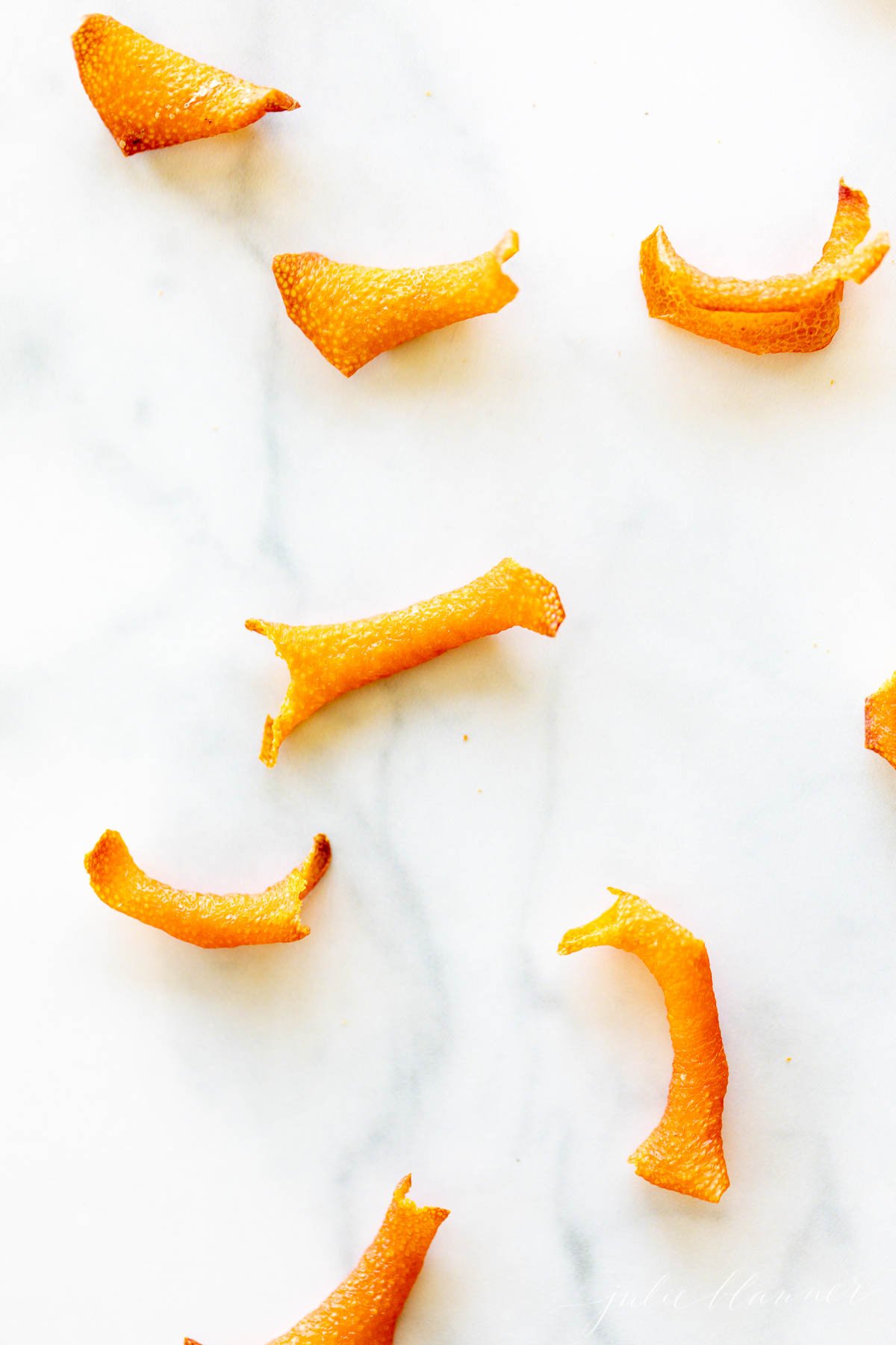 Several small, curved strips of dried orange peel are scattered on a white marble surface.