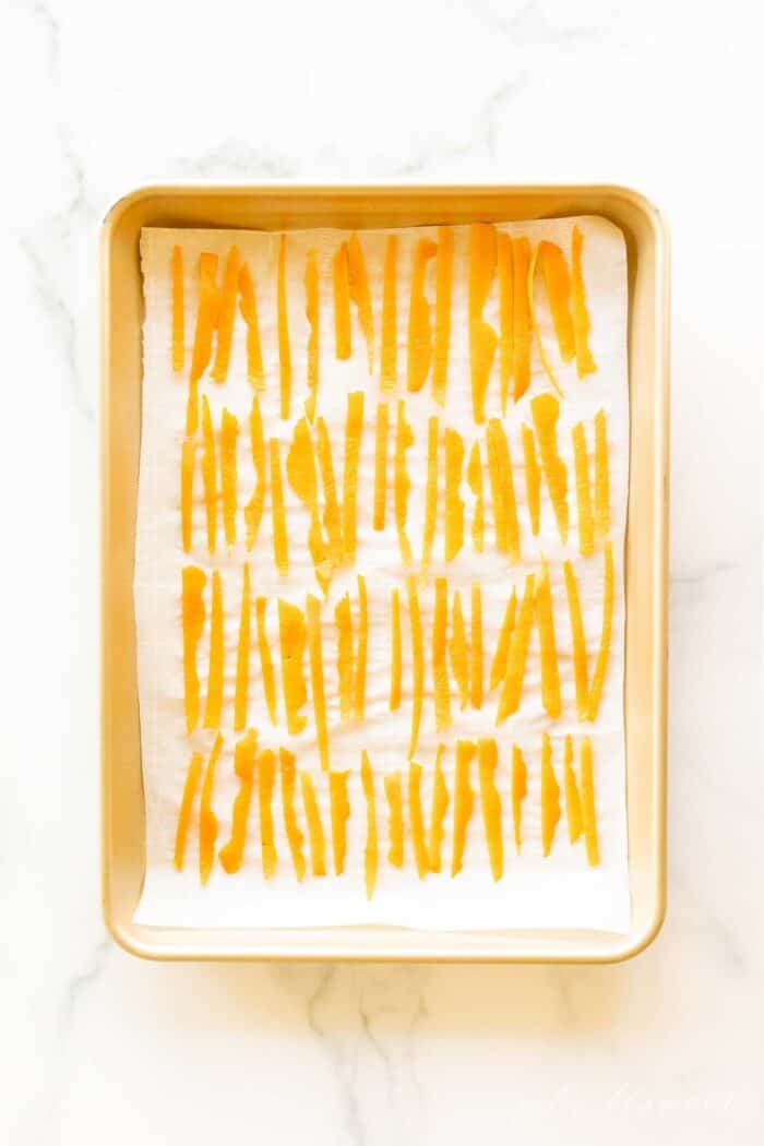 A gold sheet pan lined with parchment paper and covered in dried orange peel slices.