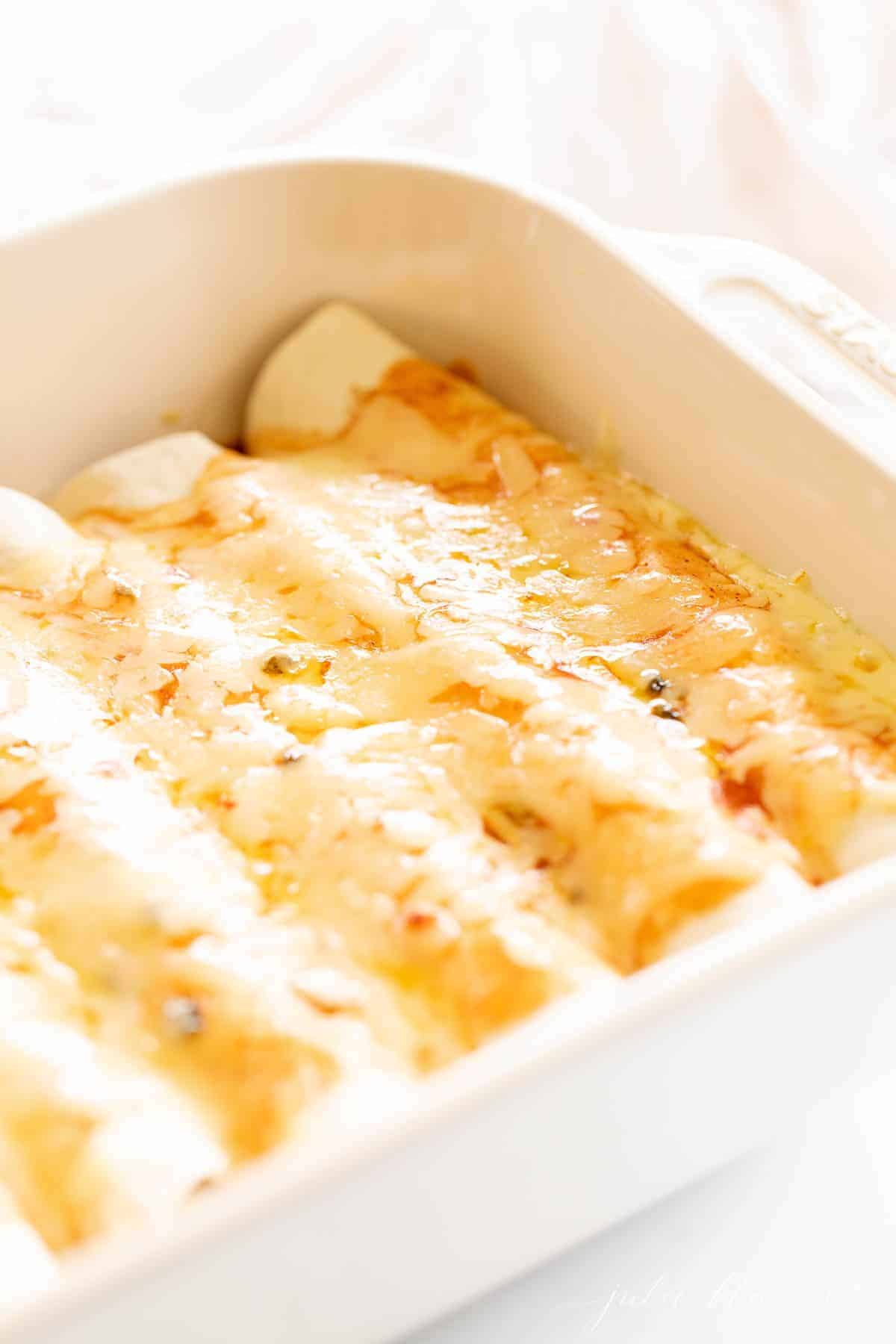 A white casserole dish filled with cheese enchiladas.