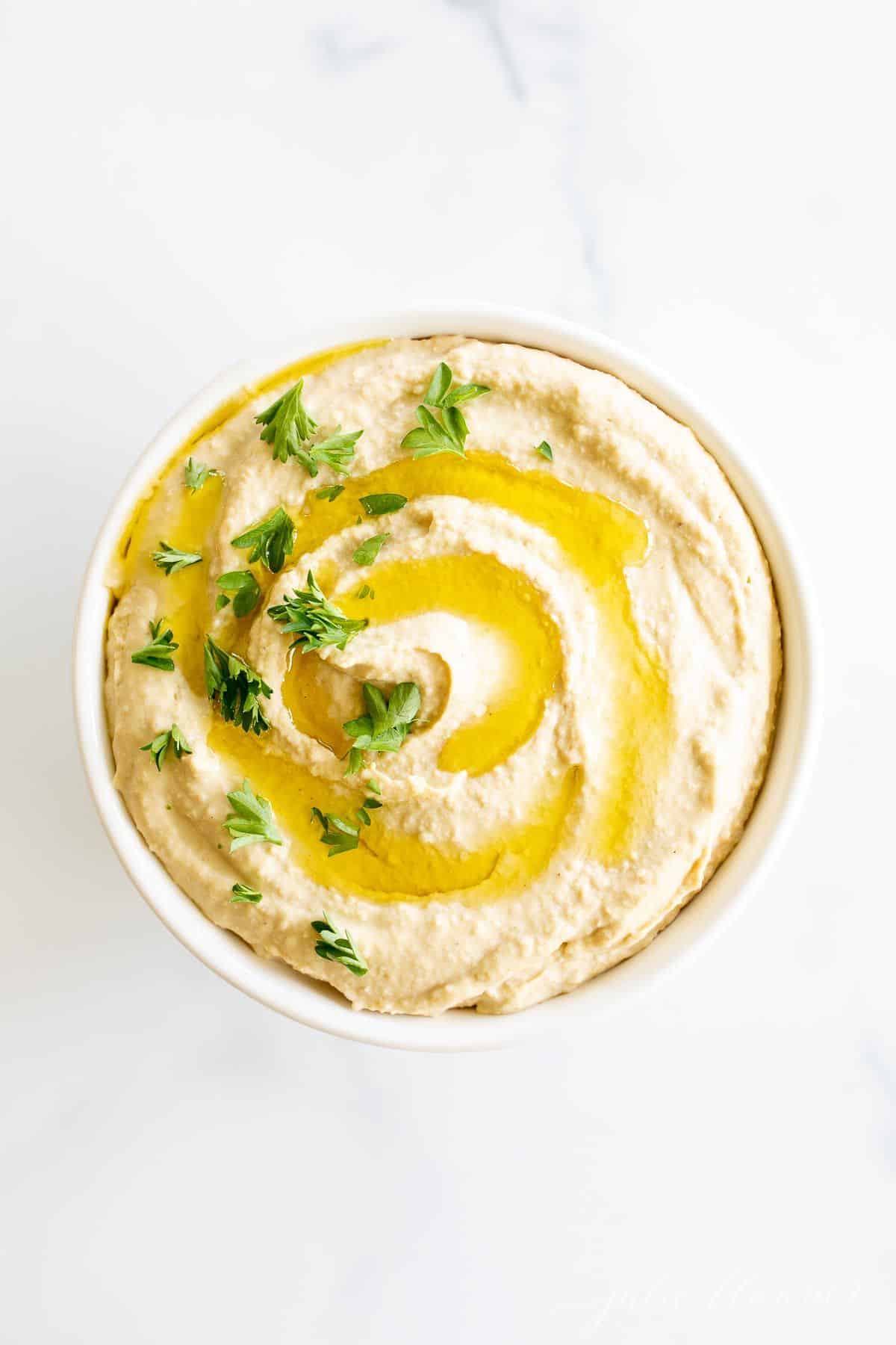 A bowl full of hummus topped with a little olive oil and parsley