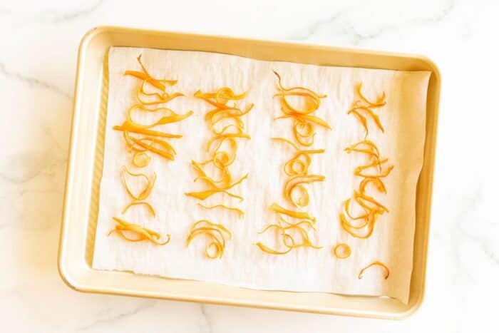 A gold sheet pan lined with parchment paper and covered in dried orange peels.