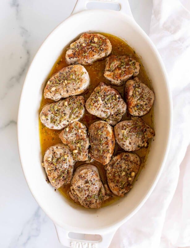 A white oval dish featuring cooked pork medallions in an apple cider glaze.