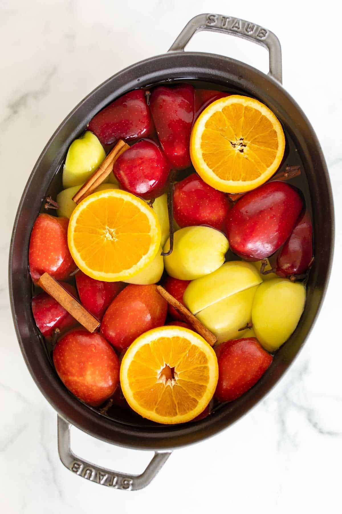 A cast iron pot filled with orange slices , apple slices and more to make a homemade apple cider recipe.