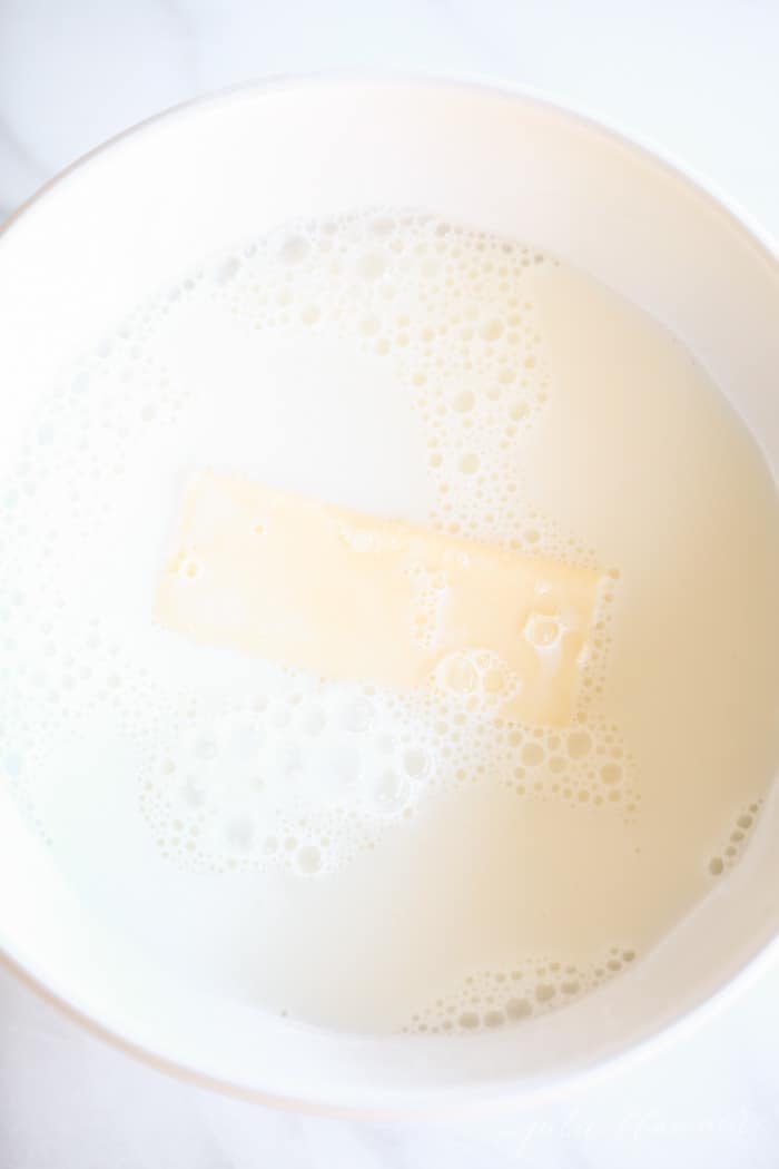 A bowl of milk with a stick of butter inside for an easy dinner roll recipe.