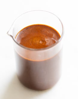 A small clear glass jar filled with enchilada sauce on a white countertop.