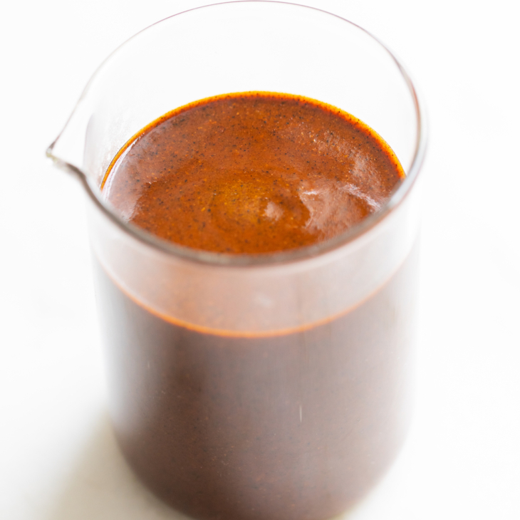 A small clear glass jar filled with enchilada sauce on a white countertop.