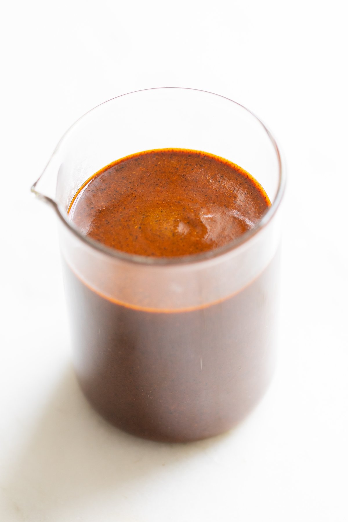 A small clear glass jar filled with enchilada sauce on a white countertop. 