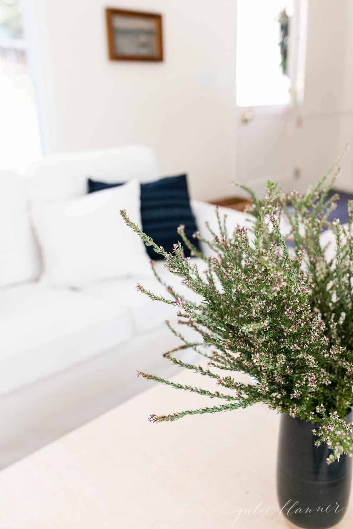 A white living room with navy pillows and a navy vase full of fall wildflowers.