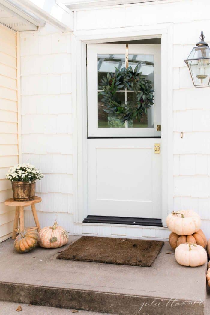 The concrete front porch of a white house with pumpkins for minimalist fall decor.