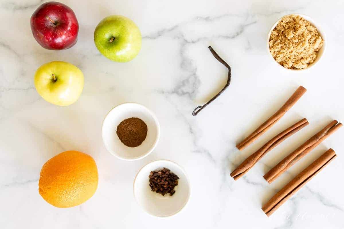 A marble surface with the ingredients for a homemade cider recipe laid out.