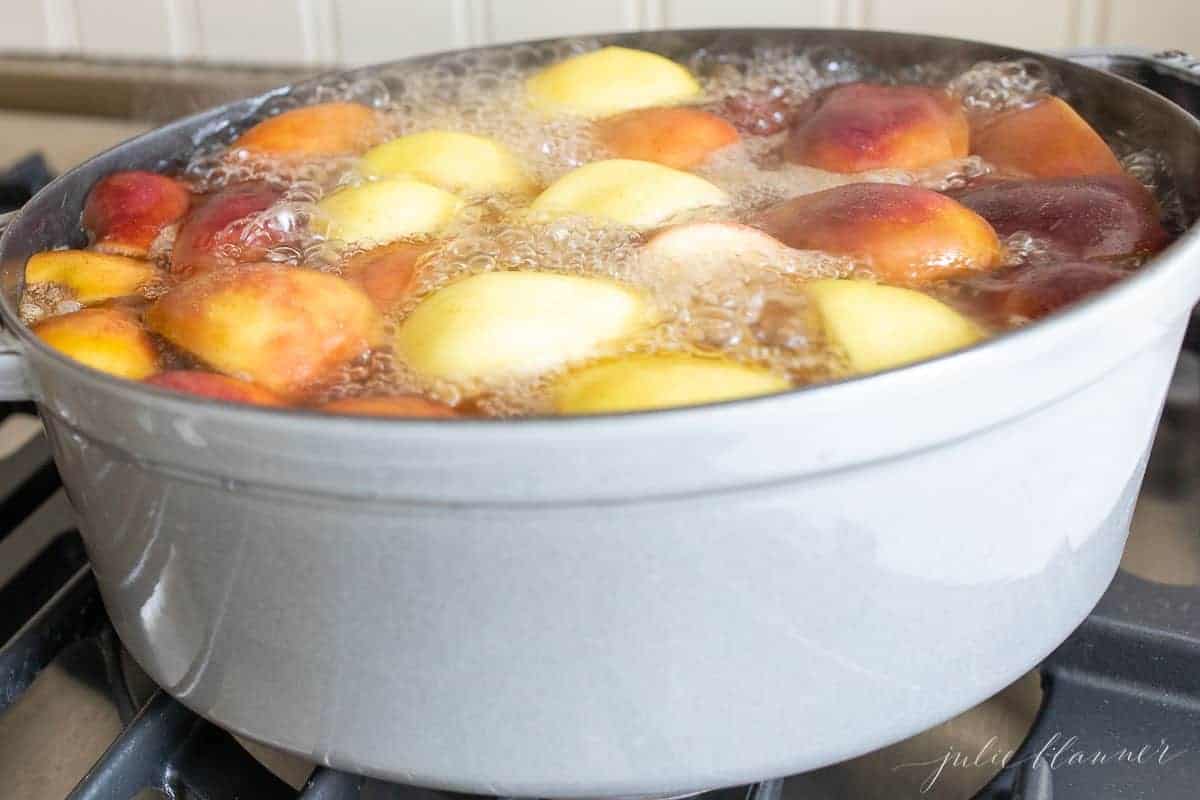 A cast iron pot filled with orange slices , apple slices and more to make a homemade apple cider recipe.