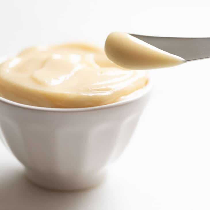 A small white bowl full of honey butter, with a knife at the corner.