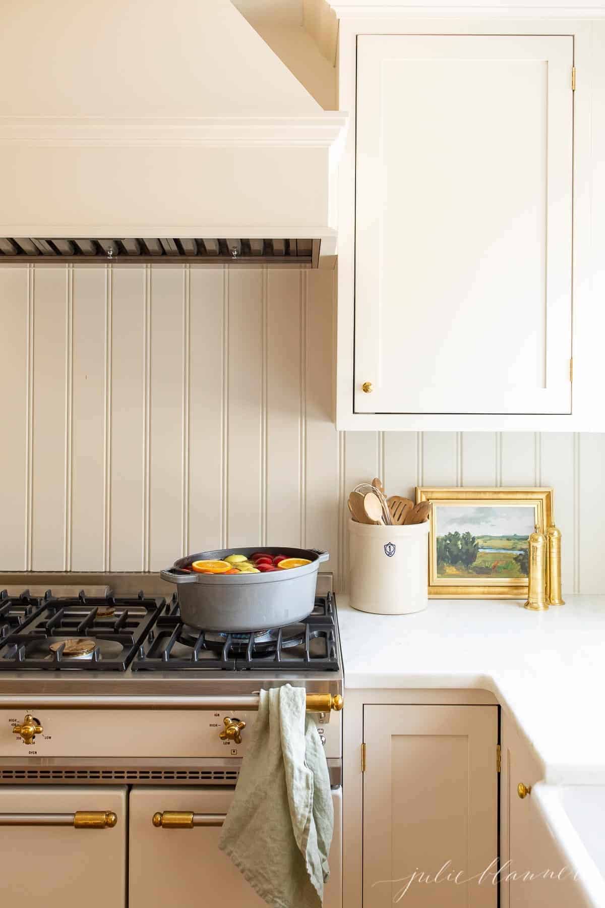 Two cast iron pots on a stove in a white kitchen filled with a homemade apple cider recipe simmering.