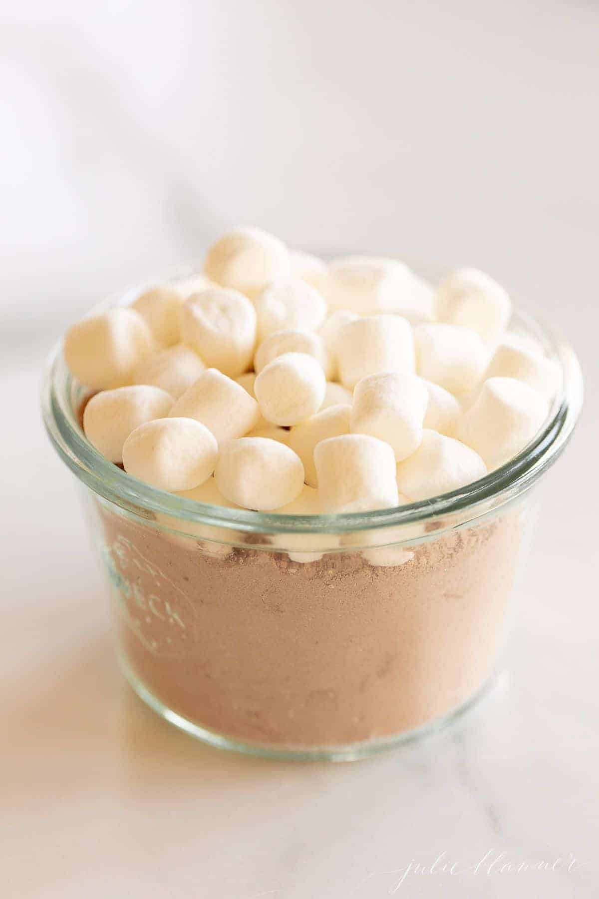 A small glass jar full of homemade hot chocolate mix topped with small marshmallows.