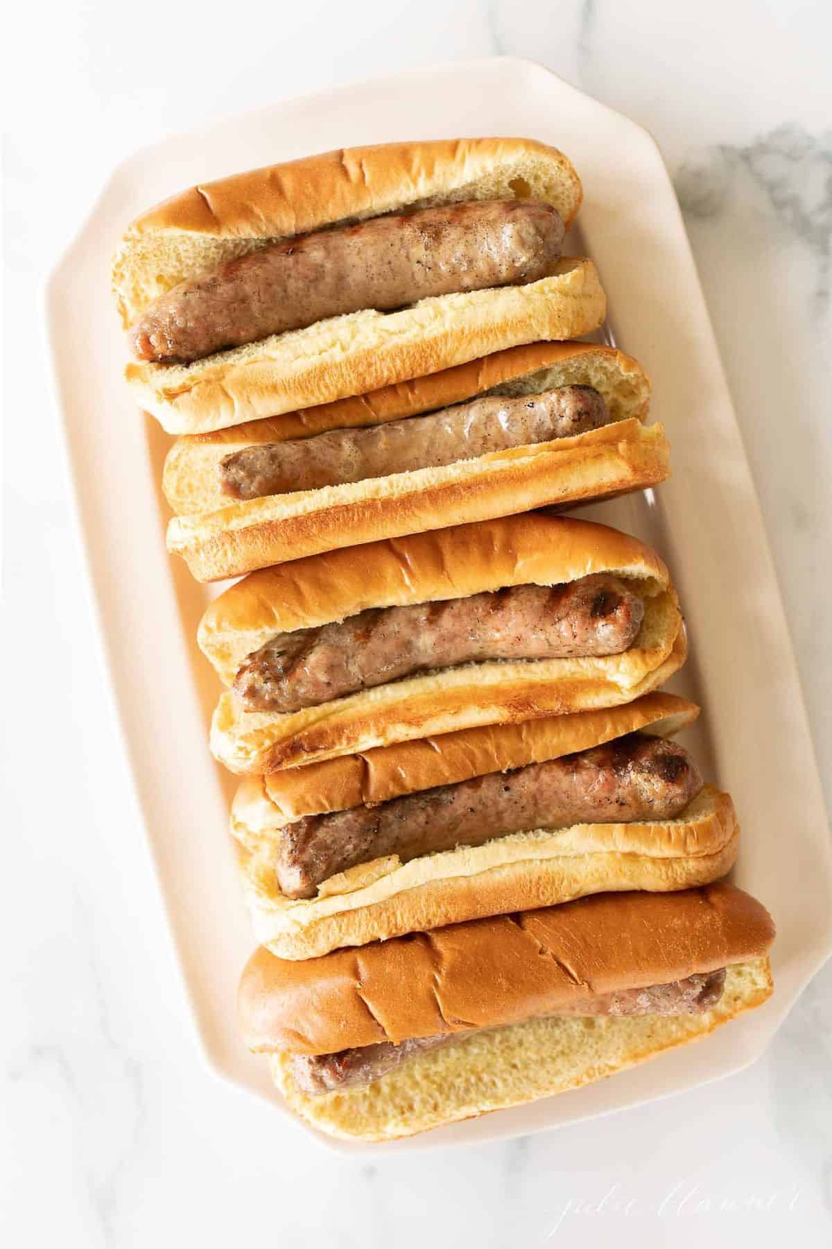 A white tray filled with bratwurst sausages in buns.