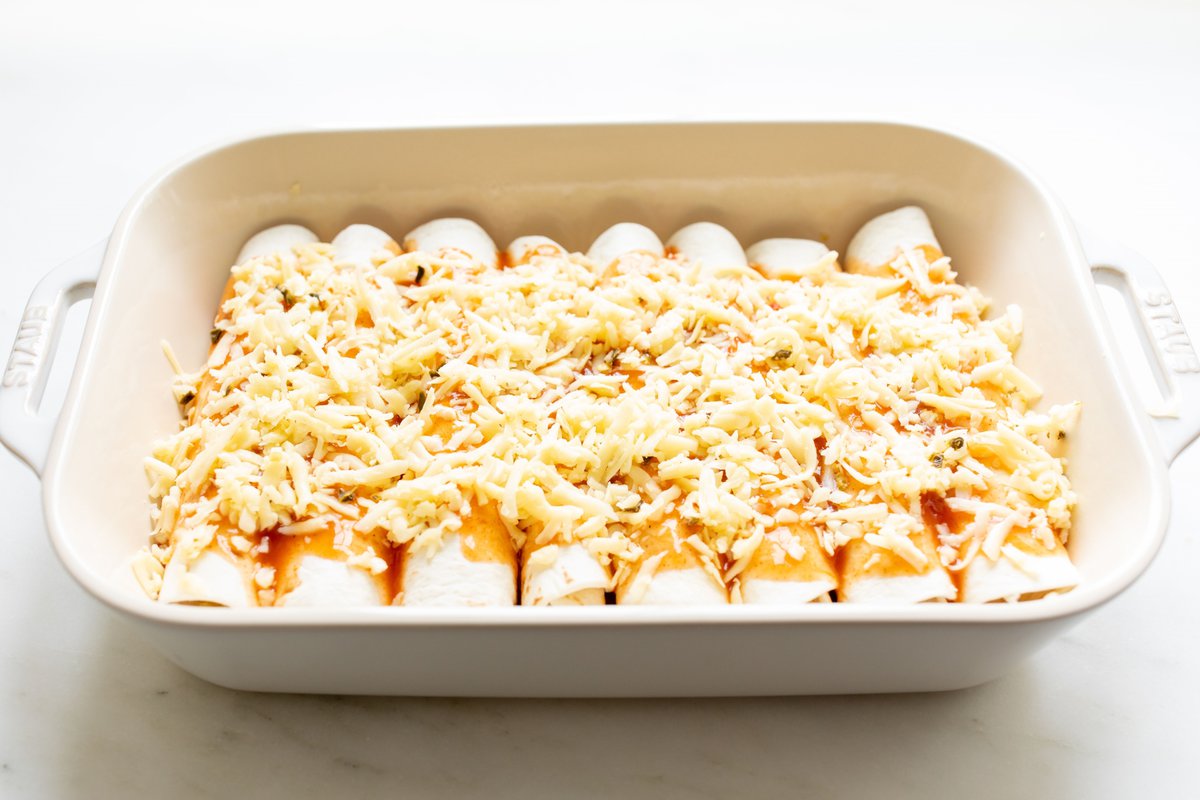 Cheese enchiladas in a white baking dish before going in the oven.