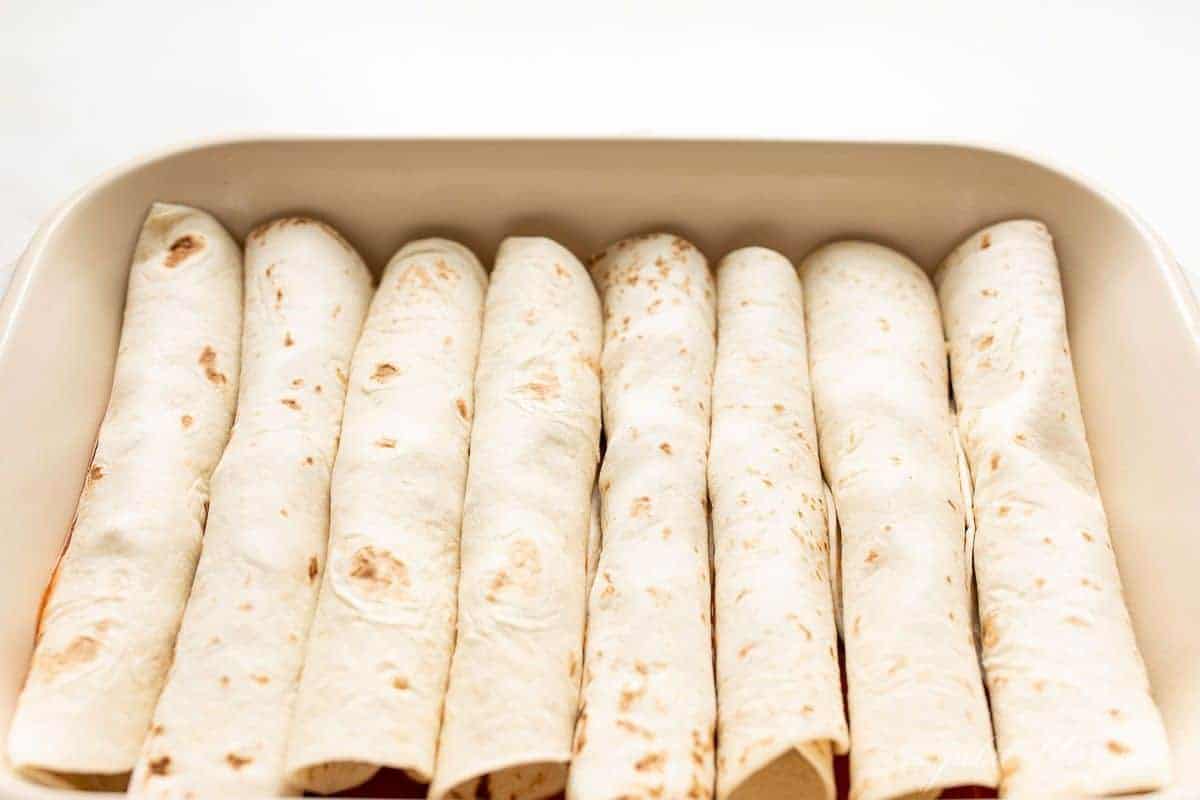 A white casserole dish filled with tortillas to make cheese enchiladas.