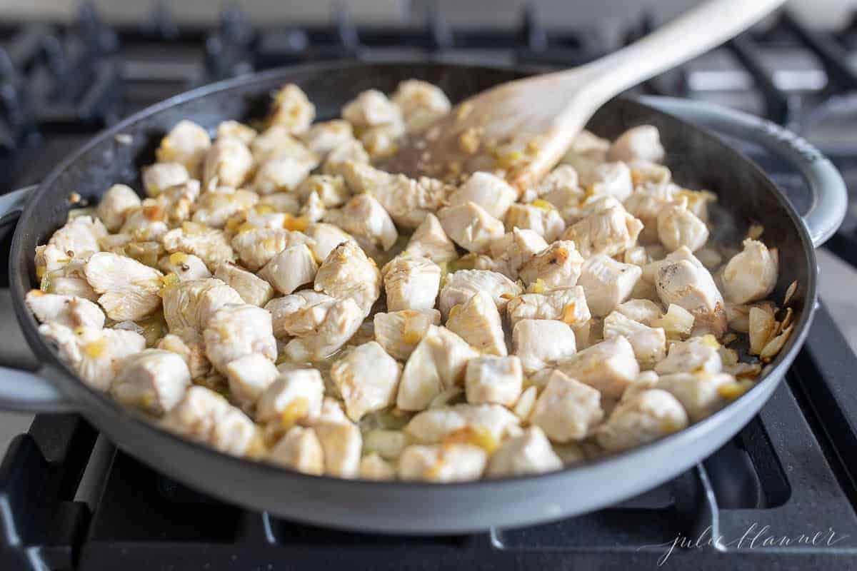 A frying pan on a stove top with cubed chicken cooking for chicken enchiladas.