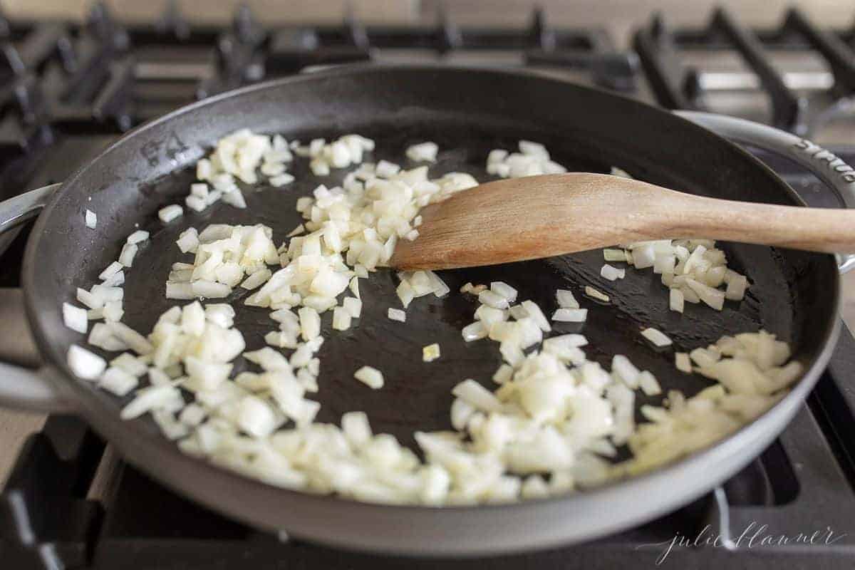 A frying pan filled with diced white onion, a wooden spatula stirring.
