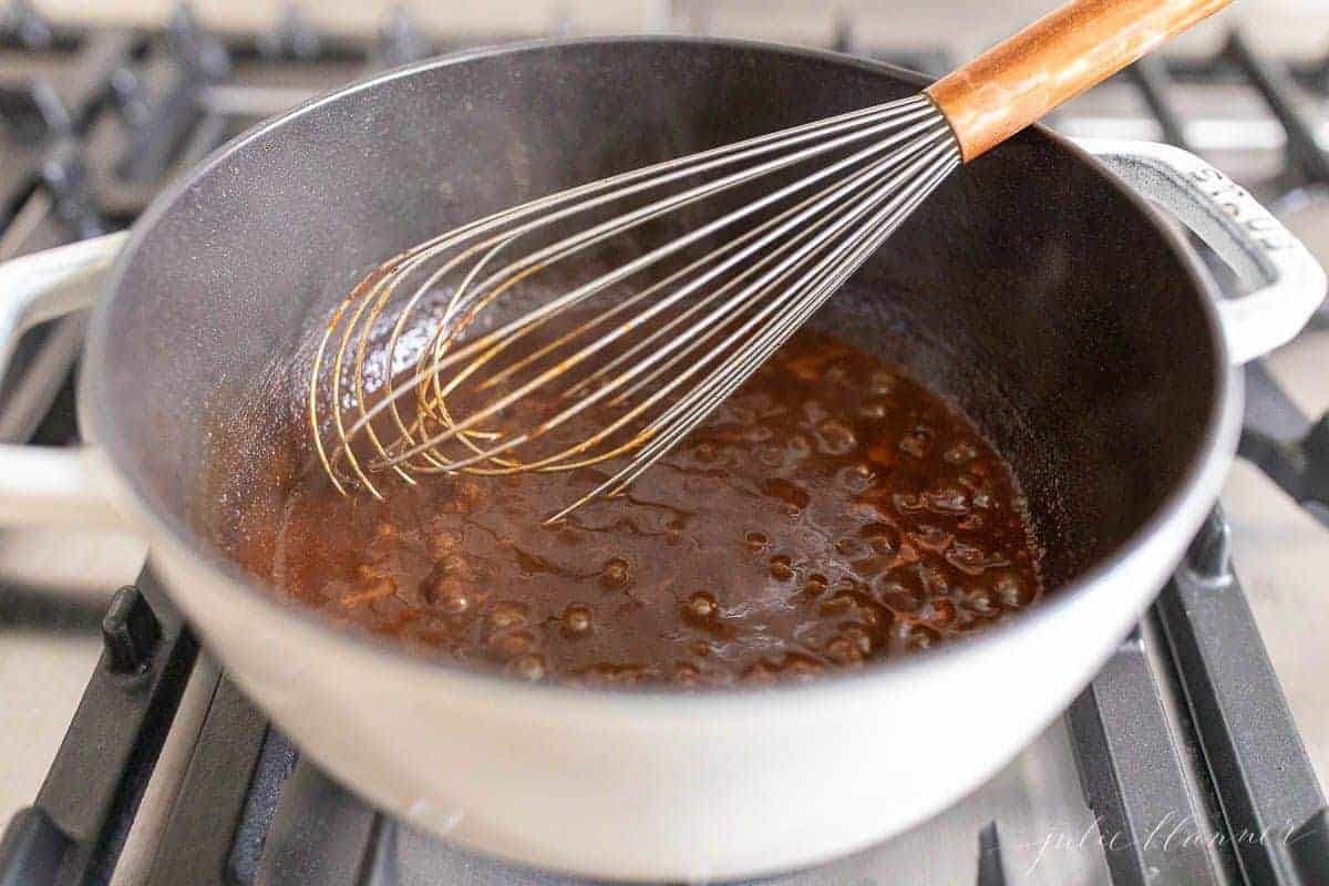 Looking into a cast iron pot full of a homemade enchilada sauce recipe on a stove top, whisk to the side.