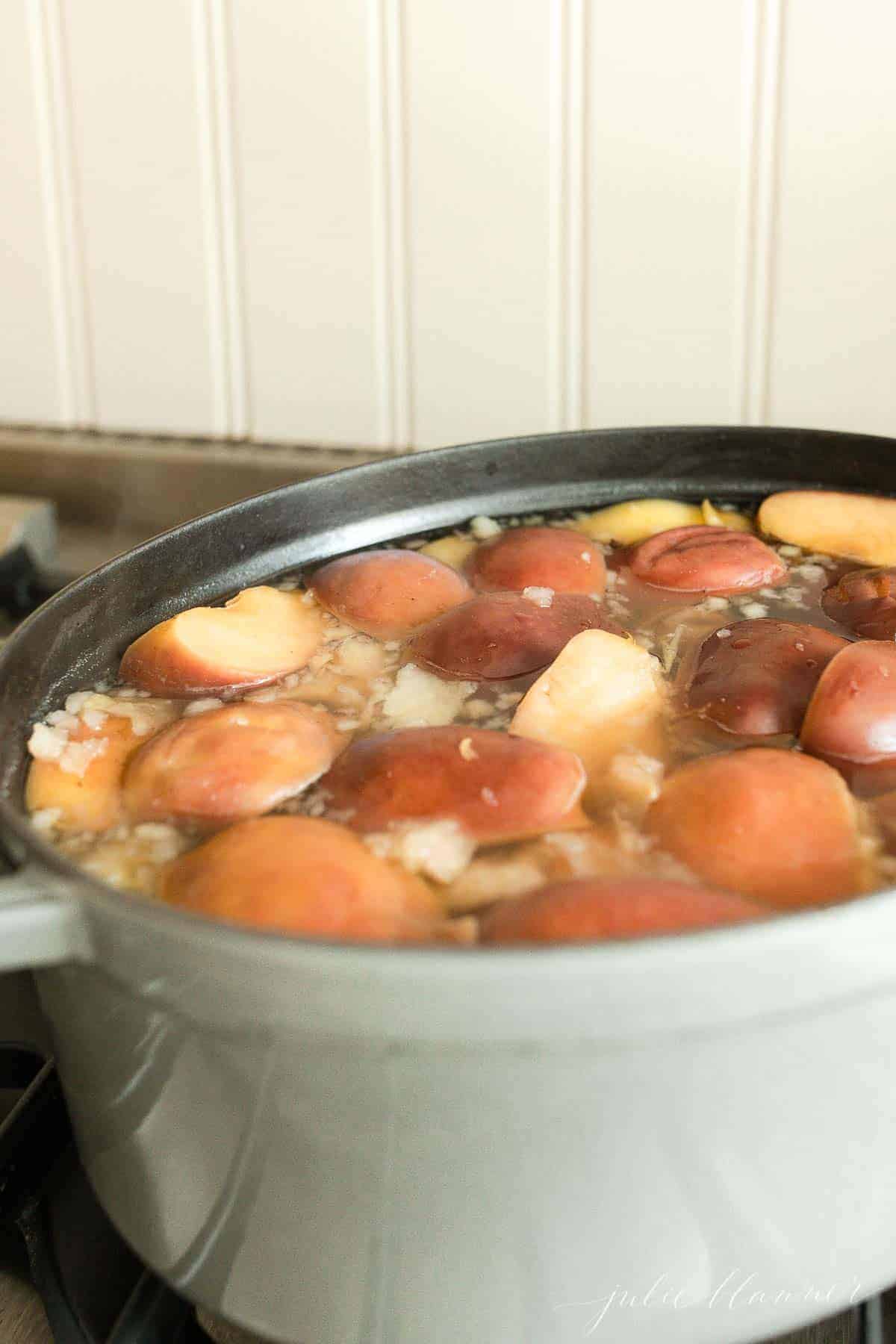A gray cast iron pan on a stove, filled with cooked apples and oranges for a homemade apple cider recipe.