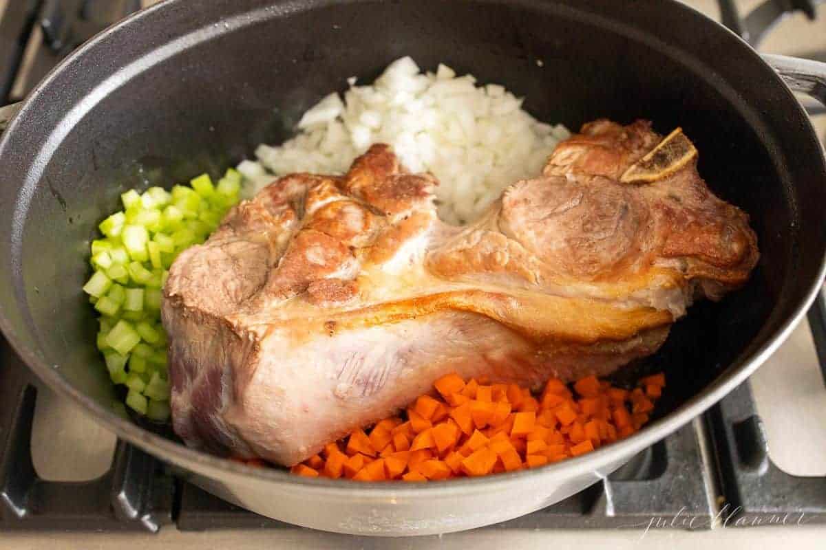 A gray cast iron pot with browned pork and vegetables inside, for pork ragu