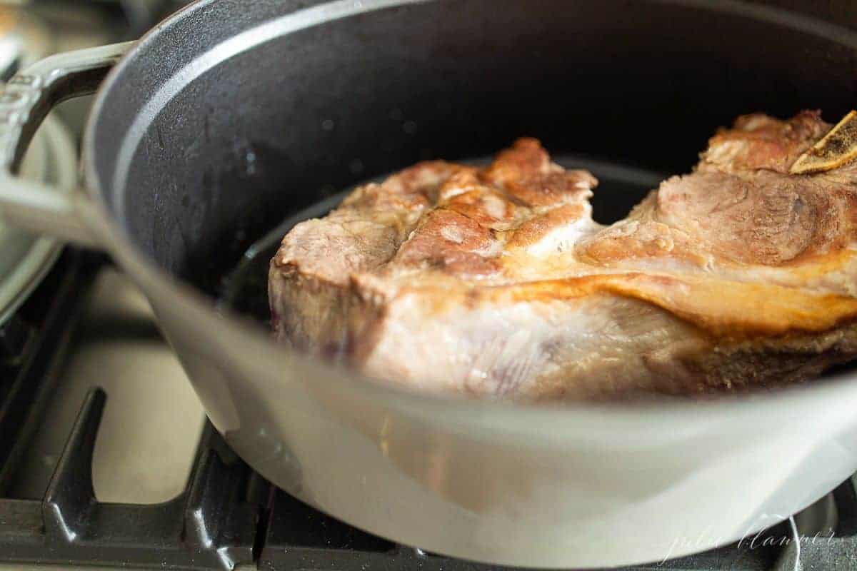  Una pentola in ghisa grigia con carne di maiale rosolata all'interno, per ragù di maiale 