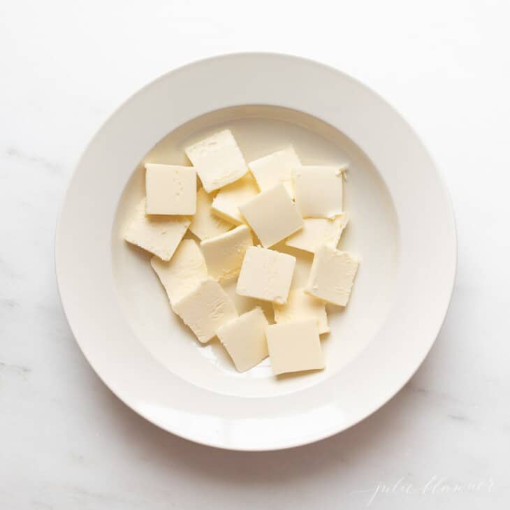 A marble surface with a white plate full of butter slices.
