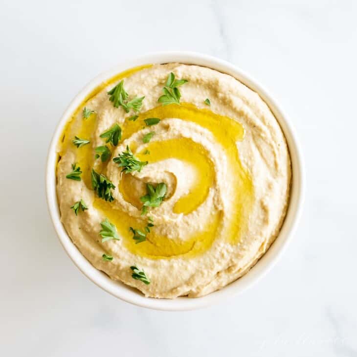 A bowl full of hummus topped with a little olive oil and parsley.