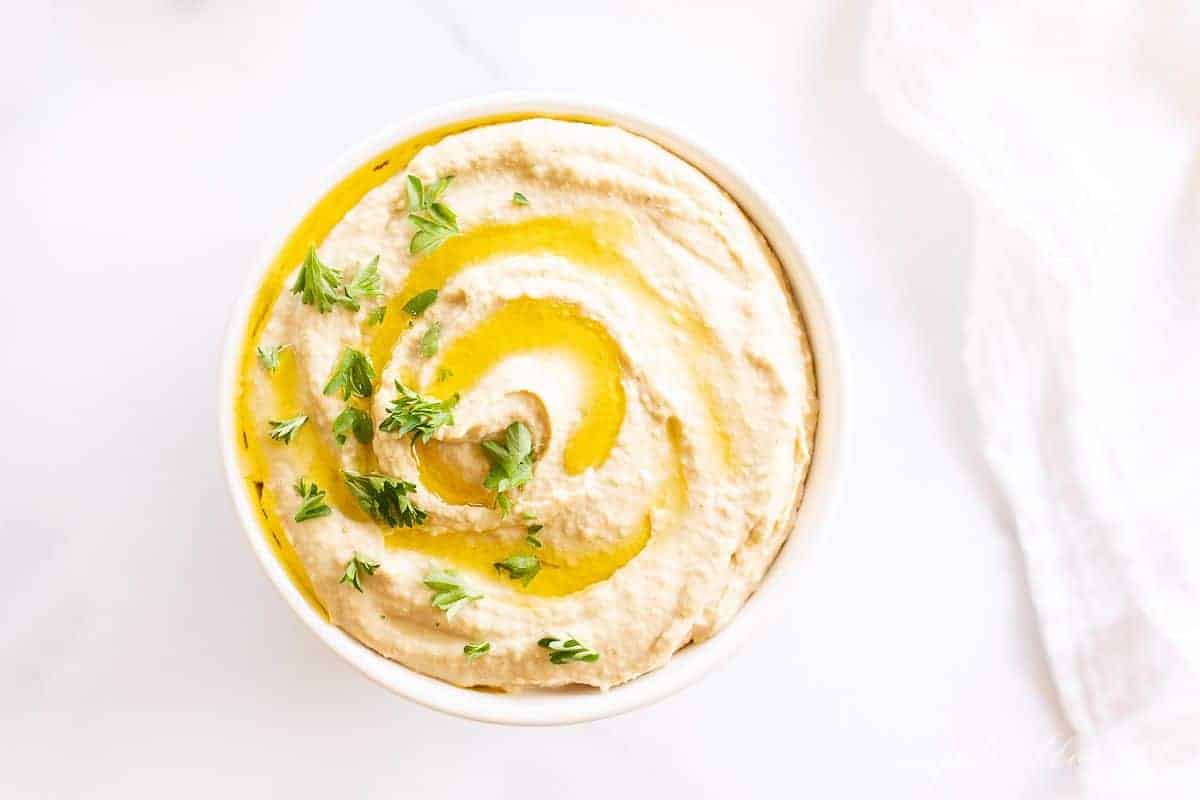 A bowl full of hummus topped with a little olive oil and parsley.