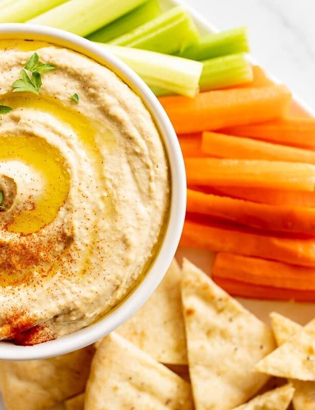 A bowl full of homemade hummus sitting on a platter of vegetables for dipping.