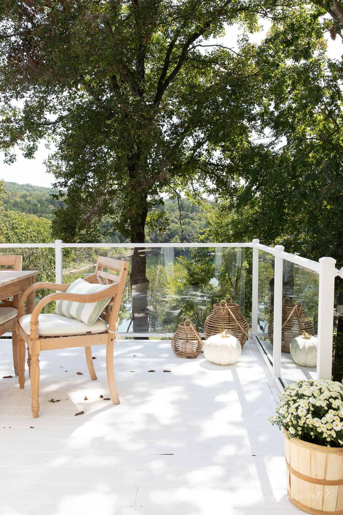 A white deck with glass railings and  white mums and white pumpkin decor.