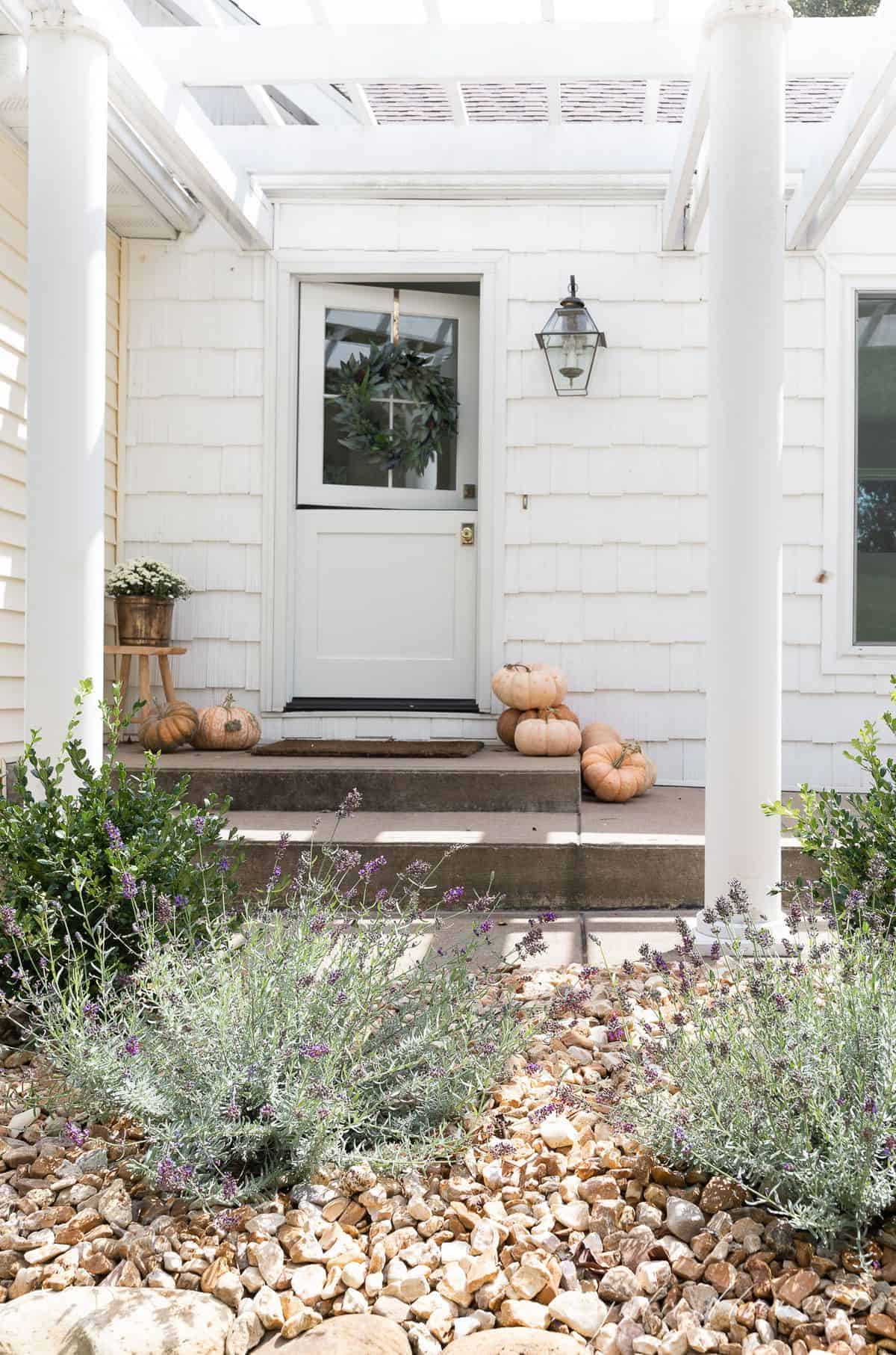 The concrete front porch of a white house with pumpkins for minimalist fall decor.