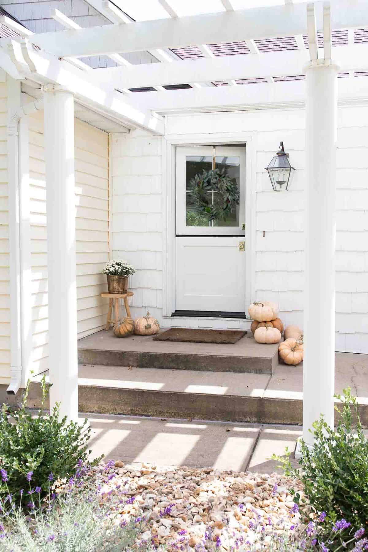 The concrete front porch of a white house with pumpkins for minimalist fall decor.