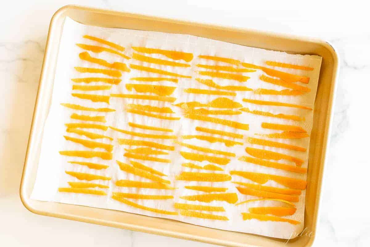 A gold sheet pan lined with parchment paper and covered in dried orange peel slices.