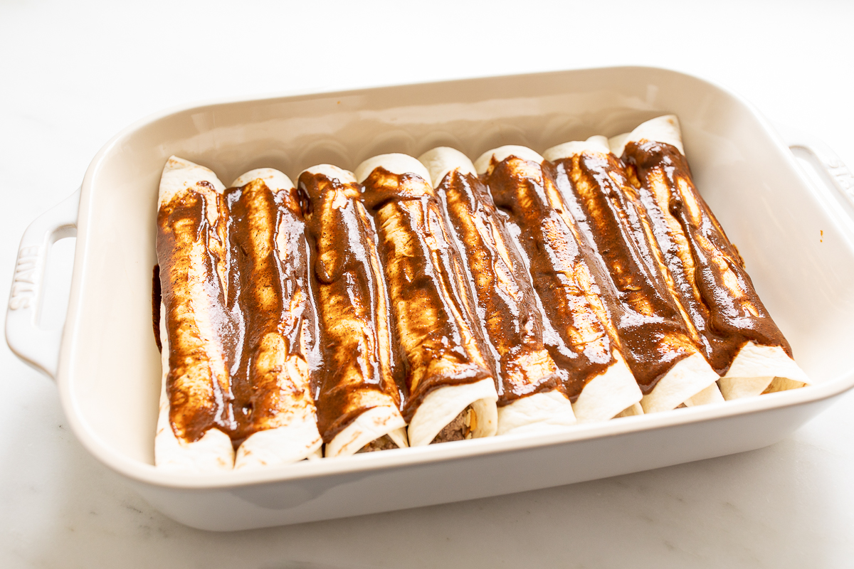 beef enchiladas in a white pan before going in the oven.