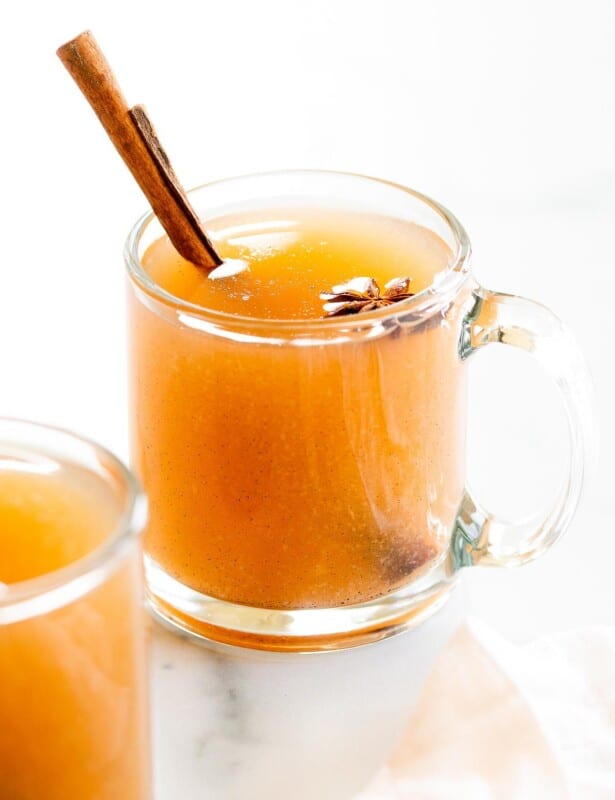 A pair of glass mugs full of pear cider, cinnamon sticks for garnish.