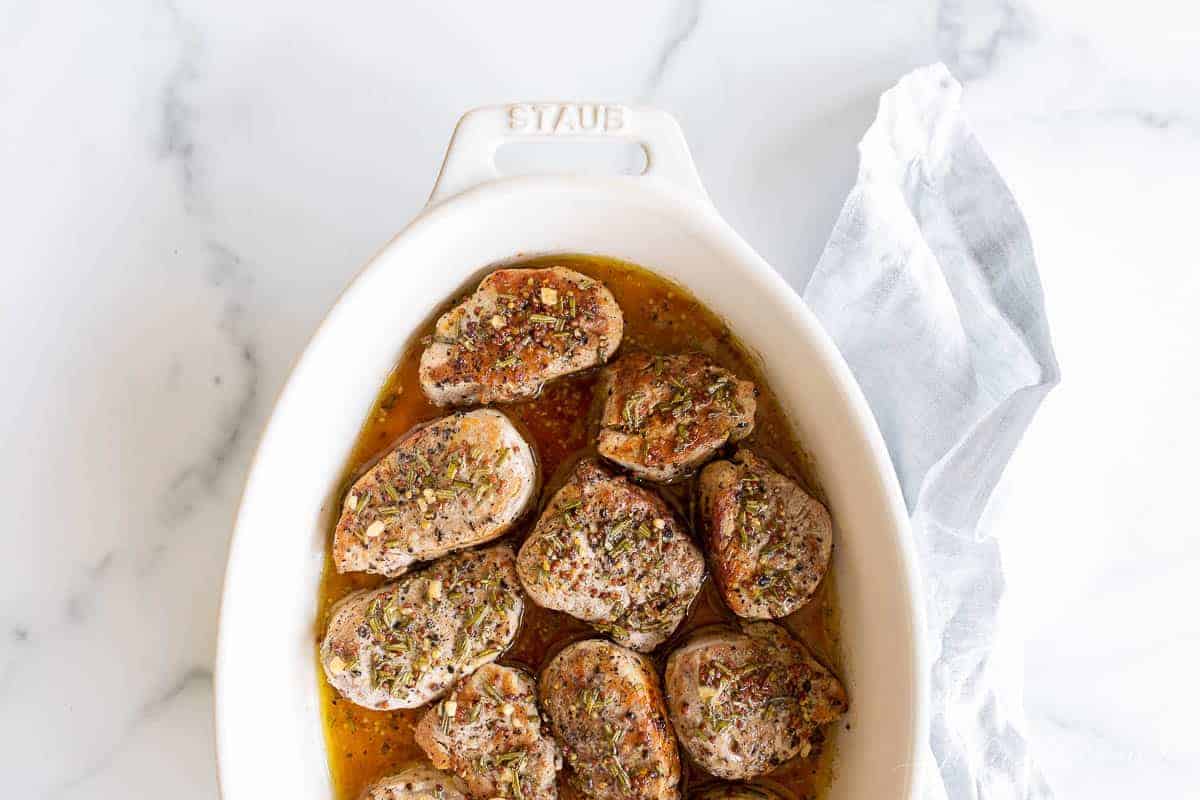 A white oval dish featuring cooked pork medallions in an apple cider glaze.